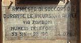 Avviso con l'indicazione dei numeri del soccorso antiaereo, visibile in un edificio del centro storico di Bologna.