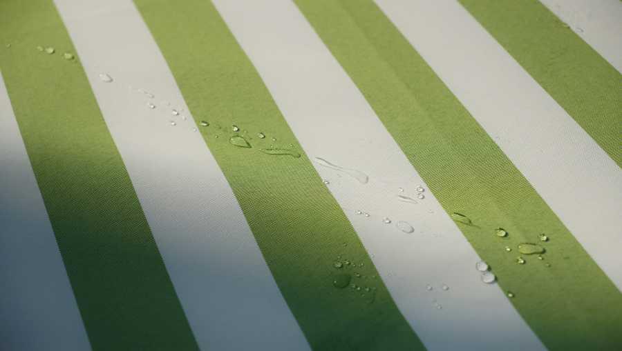 Telo rigato verde e bianco di tenda da sole con gocce d&rsquo;acqua visibili sul tessuto.