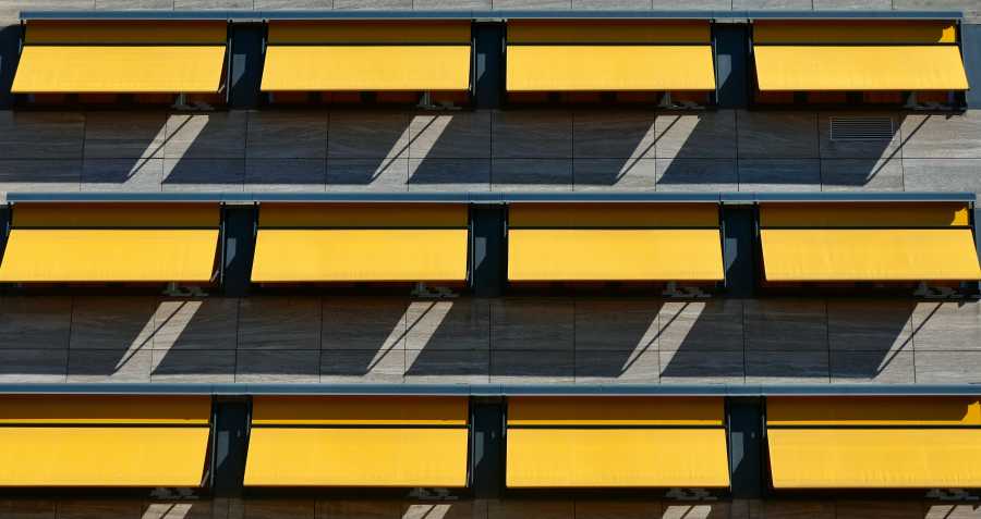 Facciata moderna con tende da sole gialle aperte e ombre proiettate sulla parete.