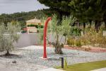 Doccia solare da giardino installata in un'area verde con pavimentazione drenante e ulivi ornamentali.