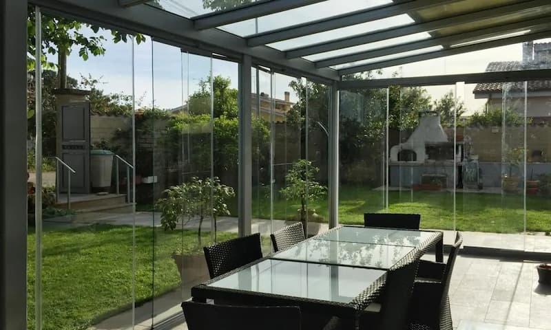 Serra bioclimatica vetrata con vista sul giardino, progettata per sfruttare la luce naturale senza rinunciare alla ventilazione.